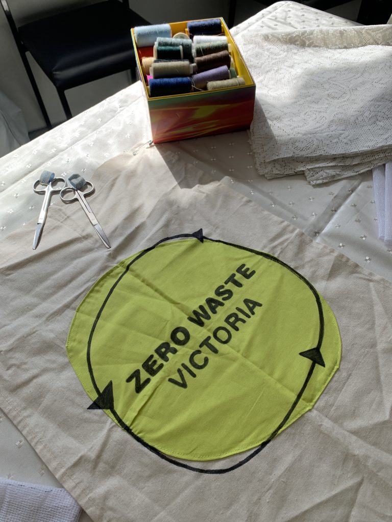 A fabric banner for Zero Waste Victoria, laid out on a table beside sewing supplies.