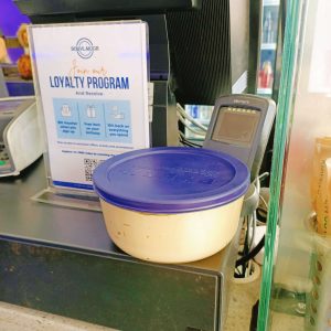 A tupperware container filled with hummus, sitting on a checkout counter.