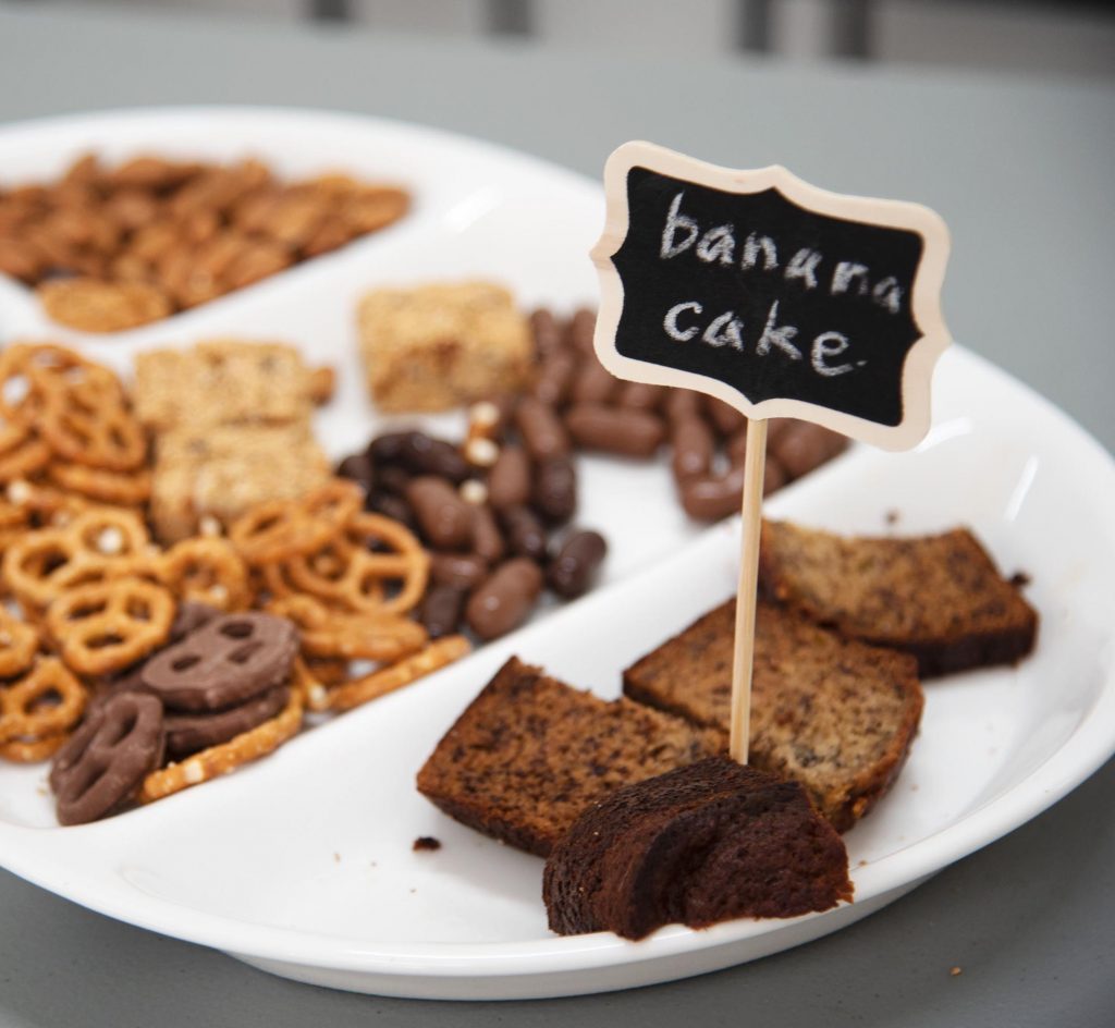 A plate of food, with a chalkboard sign sticking out of a slice of banana cake.
